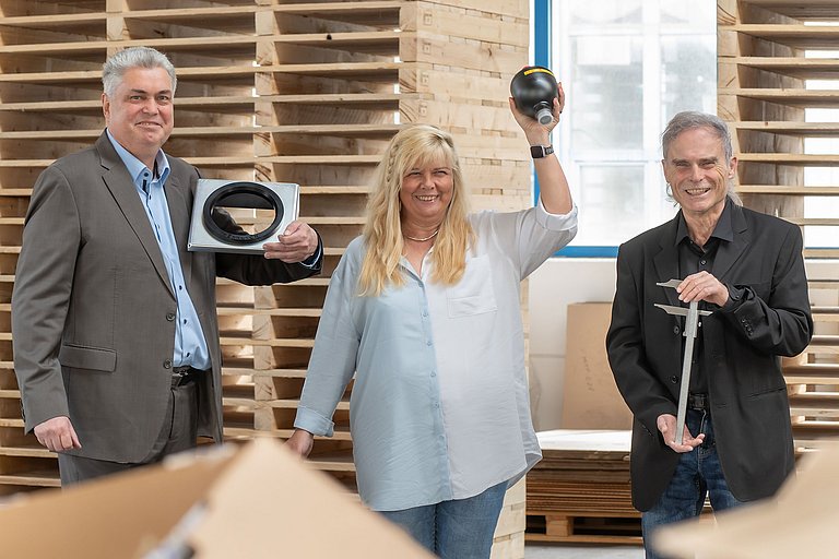 Drei Mitarbeiter schauen in die Kamera und halten eine Konsole, einen Membranspeicher und einen Messschieber