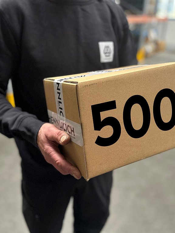 Mitarbeiter hält einen Hennlich Verpackungskarton, auf dem eine große 500 zu sehen ist