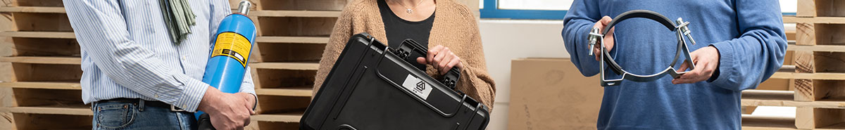 Drei Mitarbeiter halten jeweils einen Blasenspeicher, einen Fllprüfkoffer und eine Befestigungsschelle