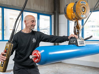 Mitarbeiter transportiert langen Blasenspeicher mittels Elektrokettenzug